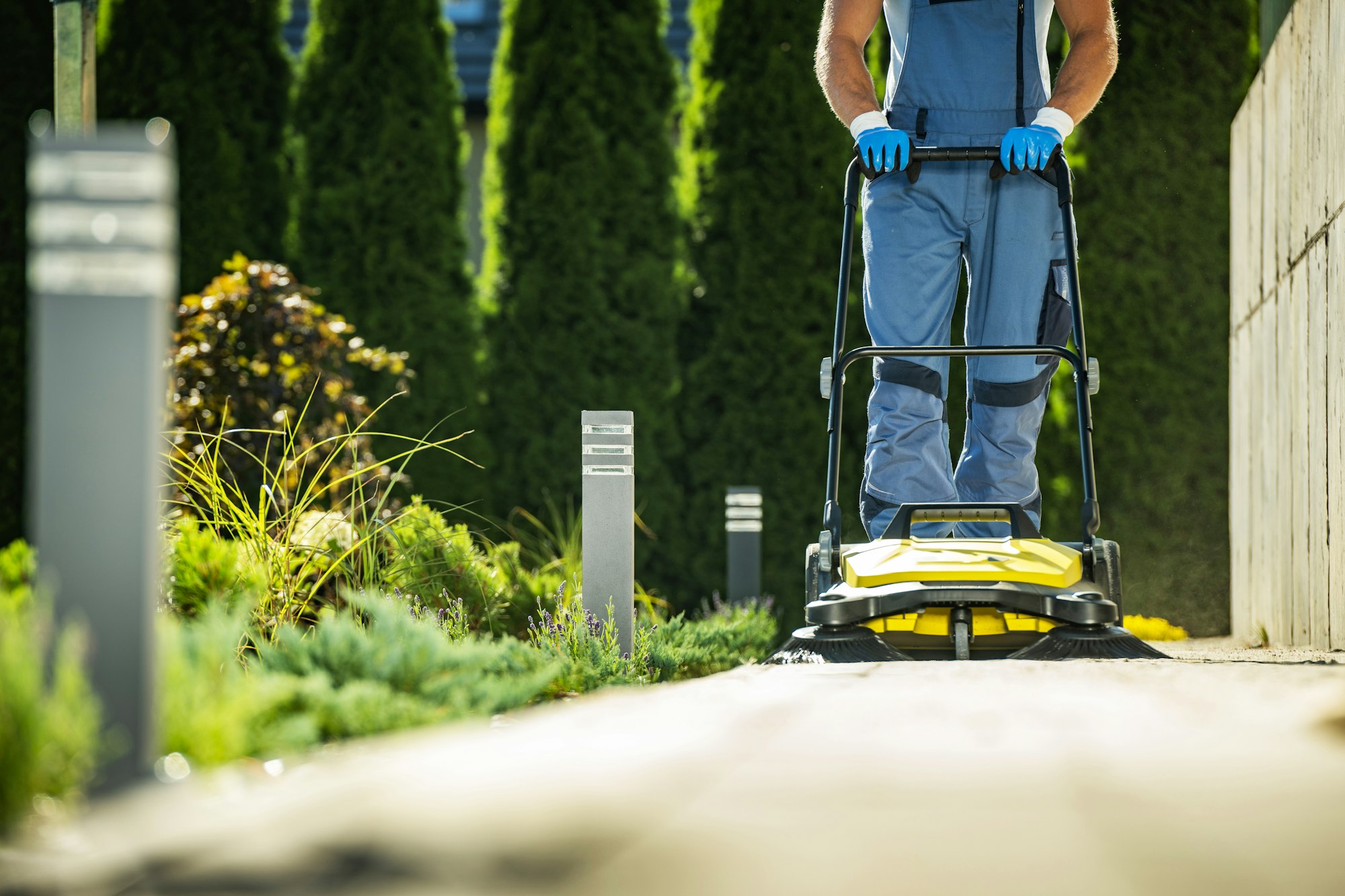 Landscaper Worker with Push Sweeper Cleaning Garden Pathway