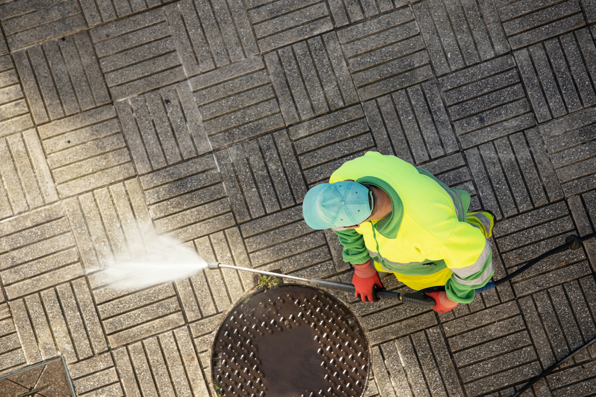 Worker cleaning a street sidewalk with high pressure water jet machine
